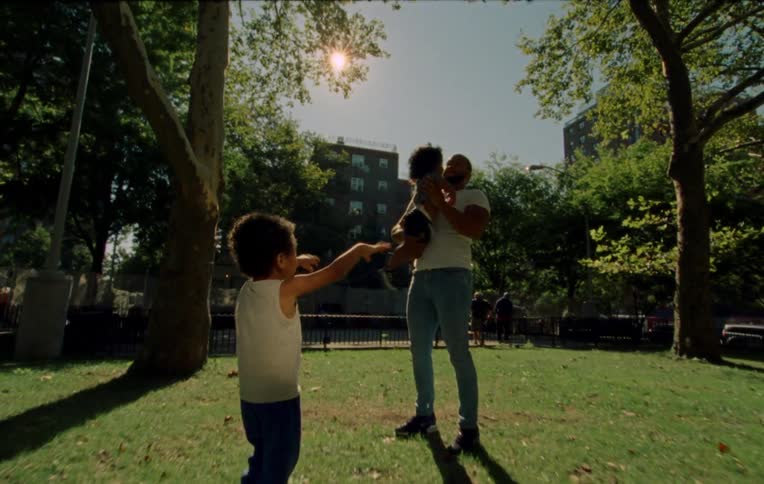 Father playing with two children one of them in his arms in an outdoor setting with grass and sunlight in the background