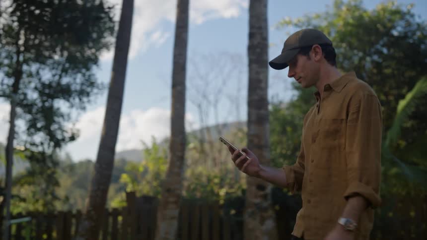 Man wearing baseball cap walks outdoors holding cellphone