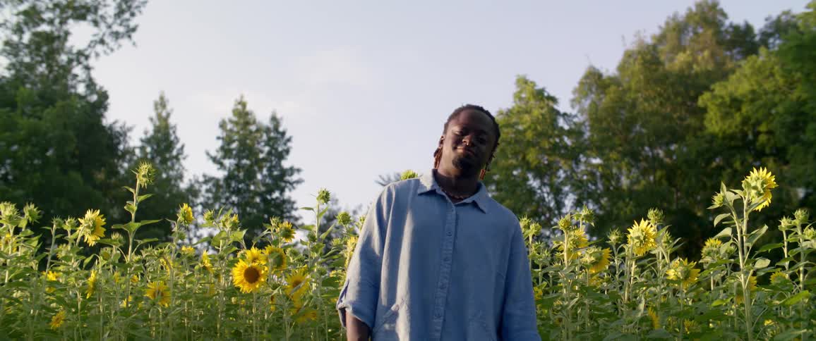A man stands on a field with sunflowers and smiles at the camera