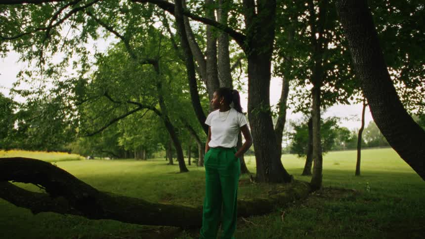 Side profile of woman wearing green pants and white shirt while standing under a tree