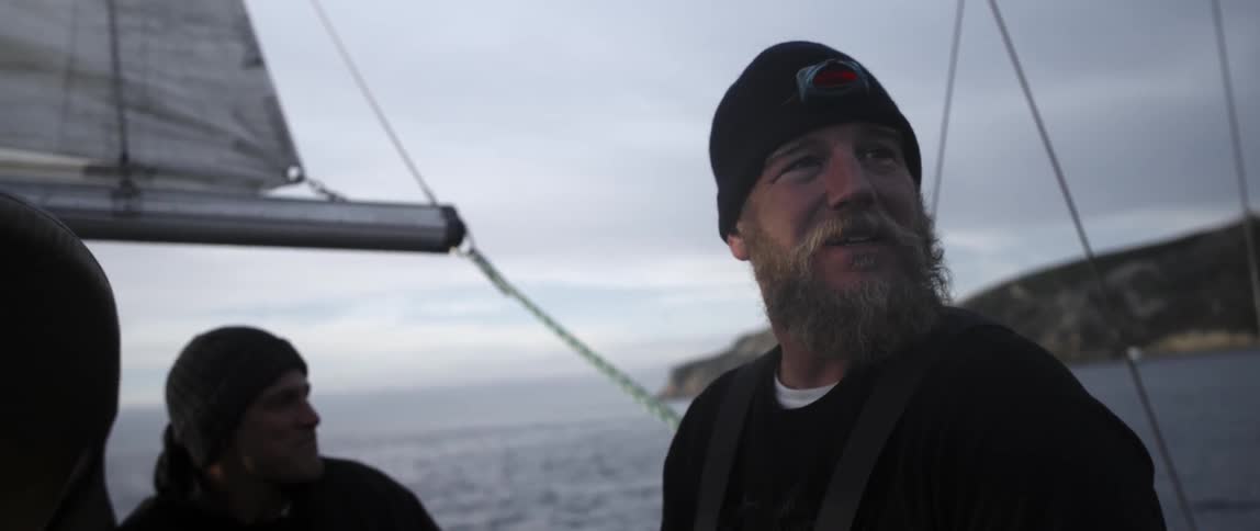 Two men talk and stand on a sailing boat together