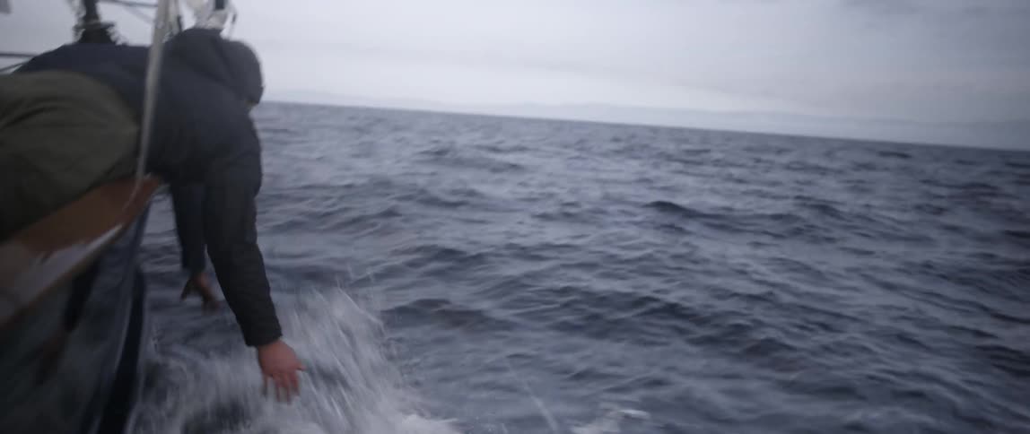 A man is handing over the side of a boat reaching for water