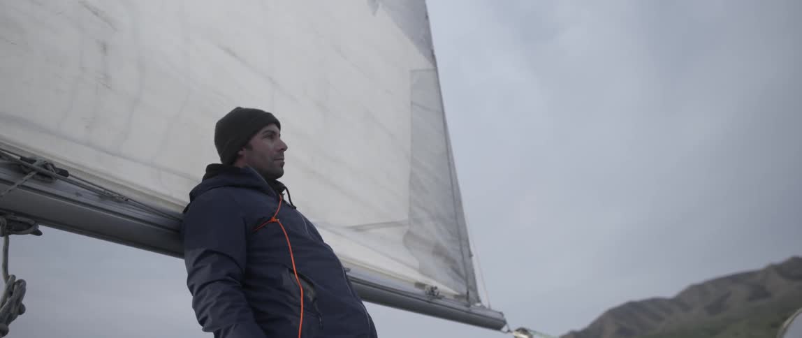 Man stands next to the sail of a boat on a cloudy day