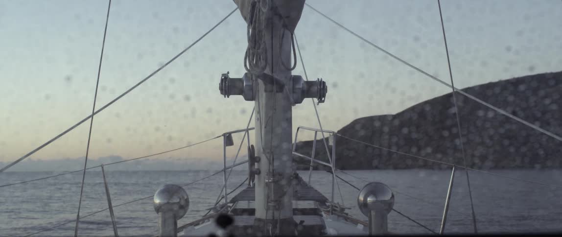 Rain is covering the window of a ship as it sails at sunset
