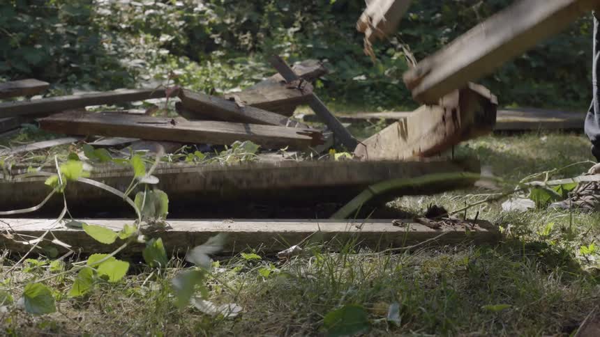 Male worker outdoors in nature setting up broken pieces of wood during day time