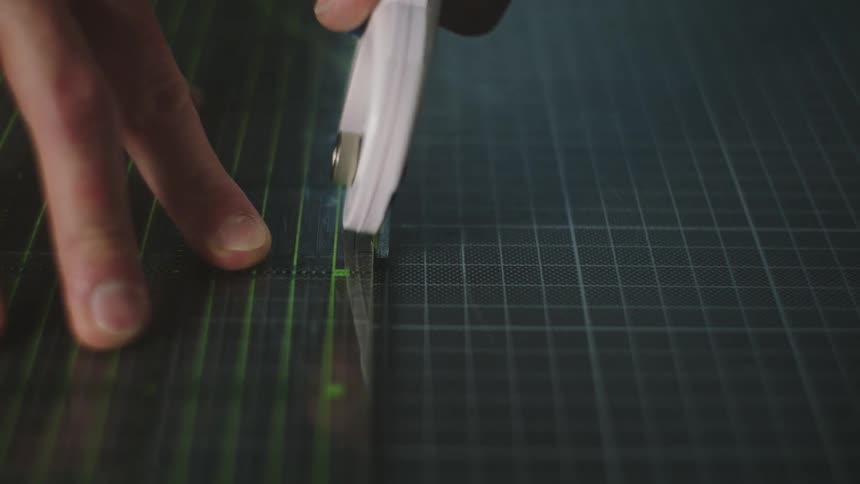 Hands of a working man at a workshop measuring and then cutting a tiny strip out of a material indoors