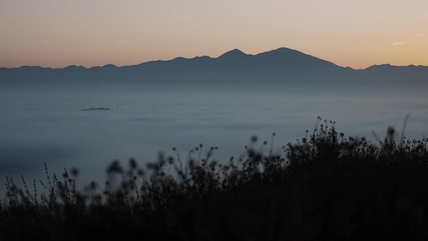 A thick layer of clouds move over a valley in between mountains