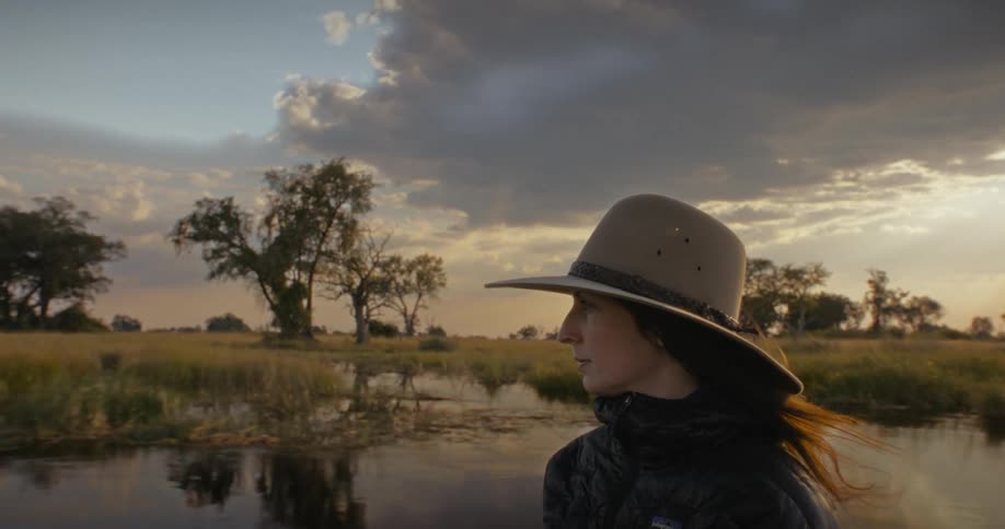 A woman rides in a boat as it crosses a wetland in the evening