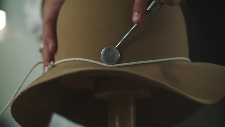 A person uses a metal tool to move a string into the hat band position on a hat