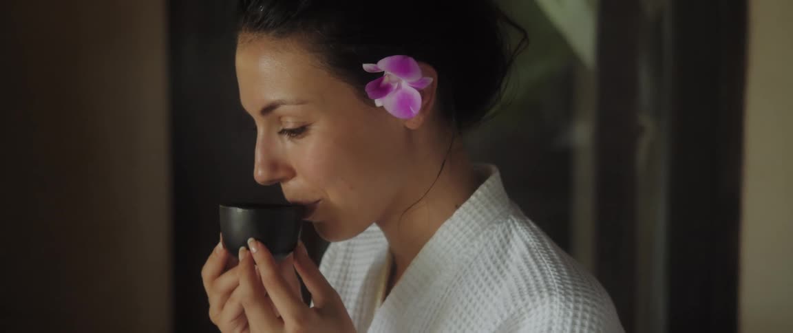 A woman is sitting in a room and drinking tea