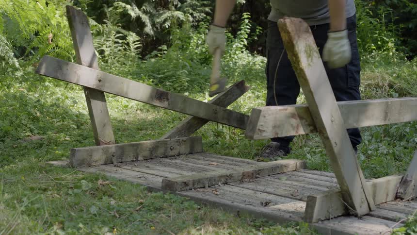 Person using gloves and a hammer breaking a wooden table in a vegetationrich outdoor environment