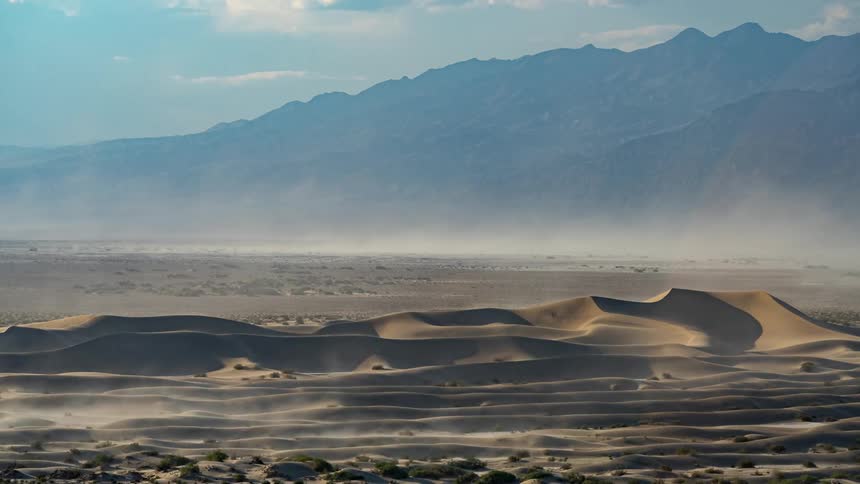 Desert with small sand dunes and a chain of mountains on the horizon