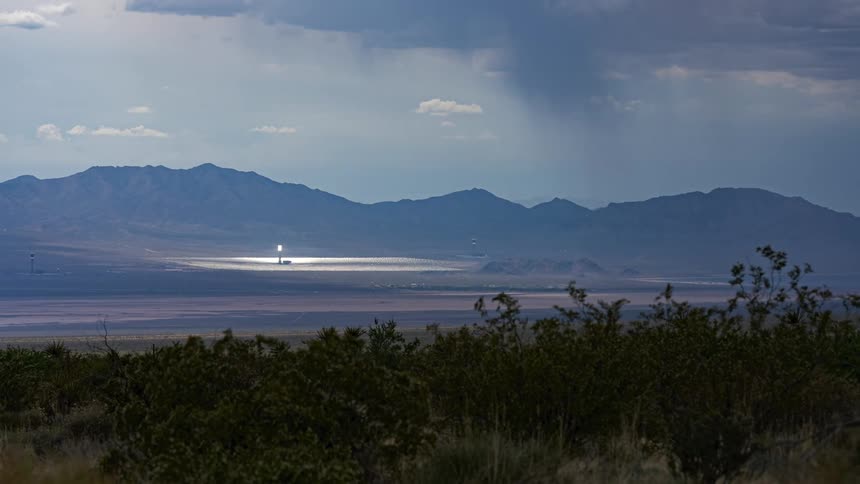 A landscape of a desert region with a streetlight illuminating an area and just behind there are mountains