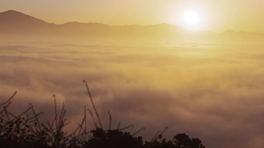 Time lapse of the sun rising over mountains on the horizon in the morning as clouds roll over the valley
