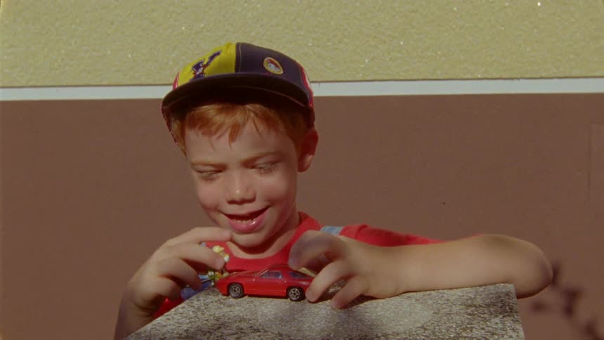 A little boy in baseball caps playing with his toy cars