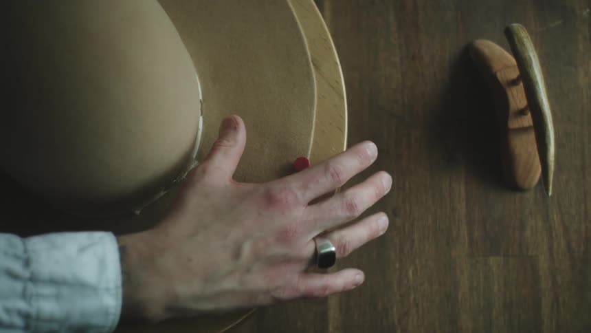 A mans hands are working on a wooden project with whittling tools next to it