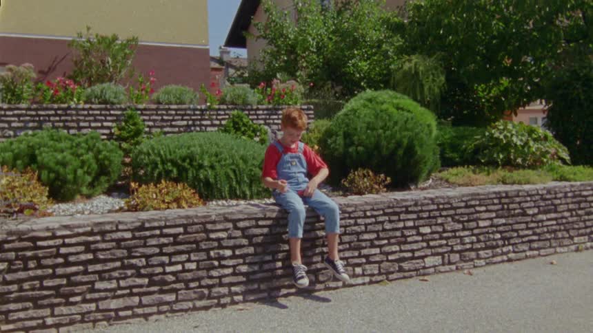 A boy sitting on a brick wall playing with his toy