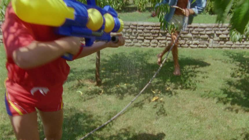 Father and child playing in the yard using toy gun and water hose during the day