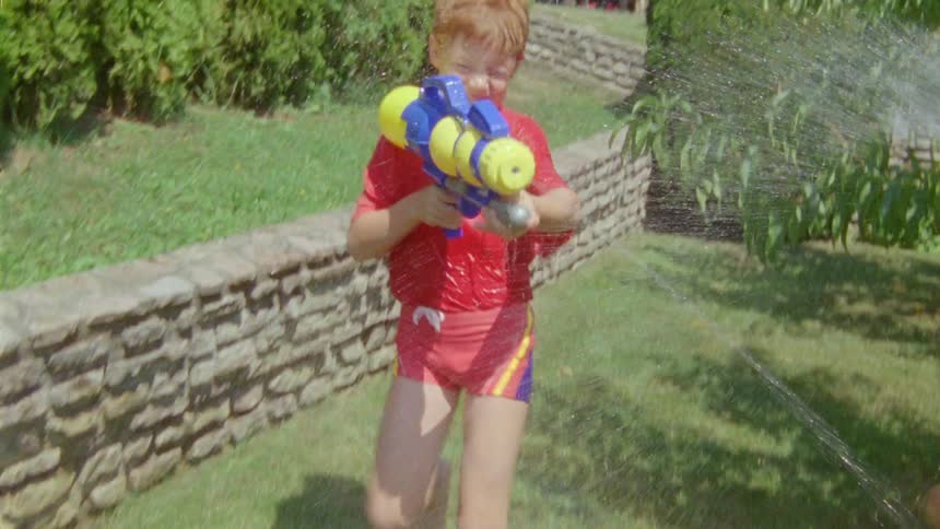 Boy and grandfather playing at the lawn throwing water at each other with a water gun and a hose during day time