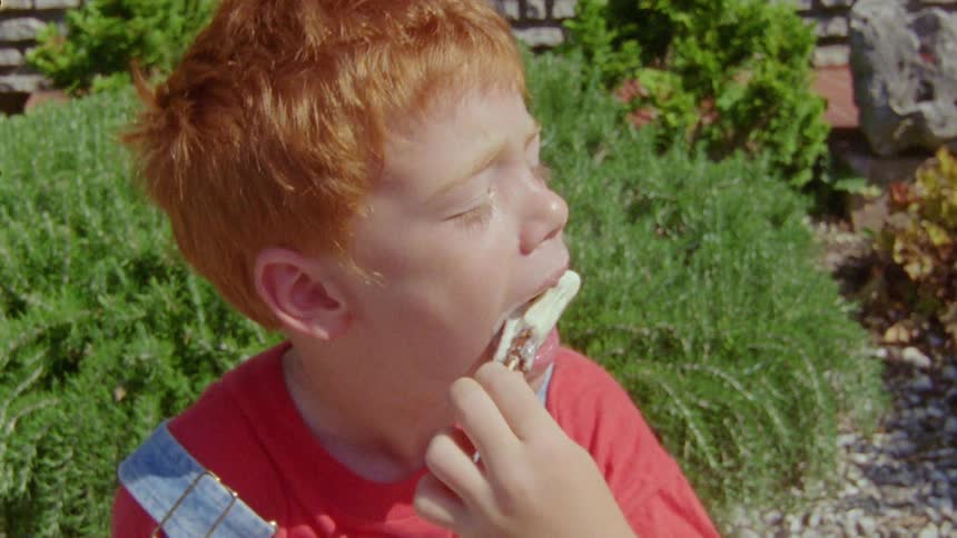 A redhaired boy sucking on a white popsicle