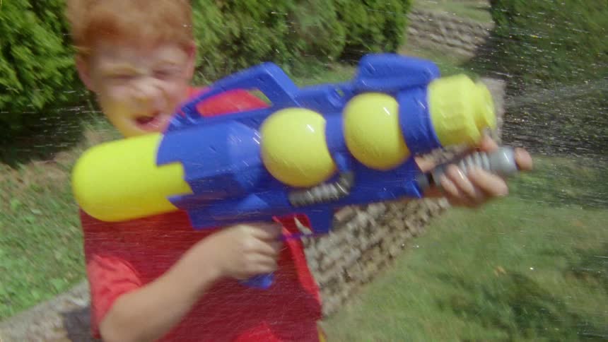 A boy plays with a water gun in a garden on a sunny day