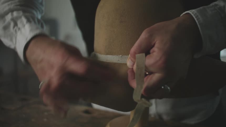 A man with rings on his fingers threading a ribbon over a hat and securing it with a nail