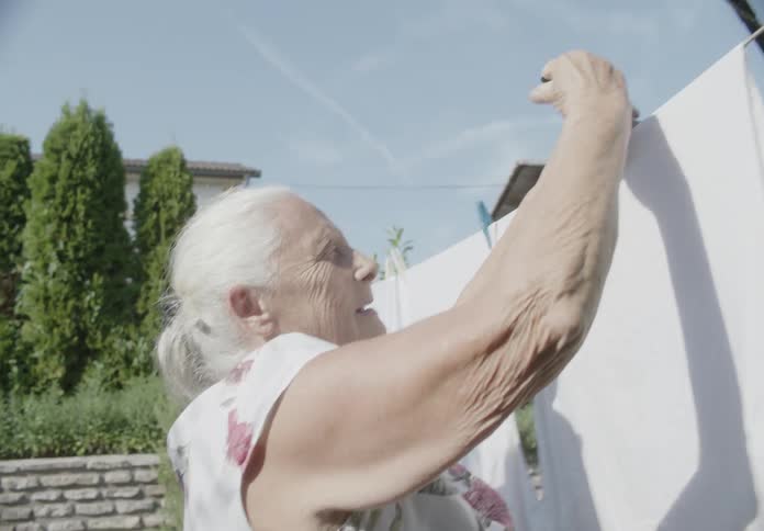 An elderly woman hanging white clothes on a clothesline