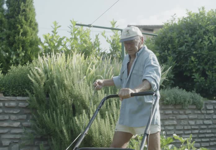 Elderly person in a yard trying to start the lawnmower