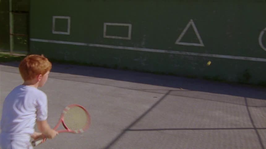 Young boy playing tennis alone at the backyard on a sunny day