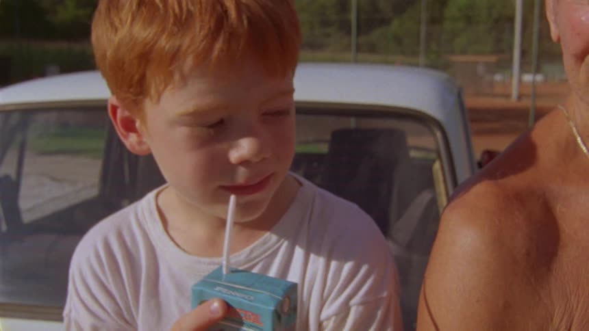 Close up of a young boy drinking out of a juice box and then handing it to his grandfather next to him