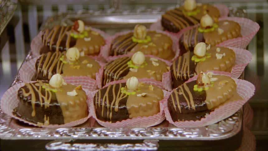 Chocolate frosted petit four cakes sit in pink baking cups