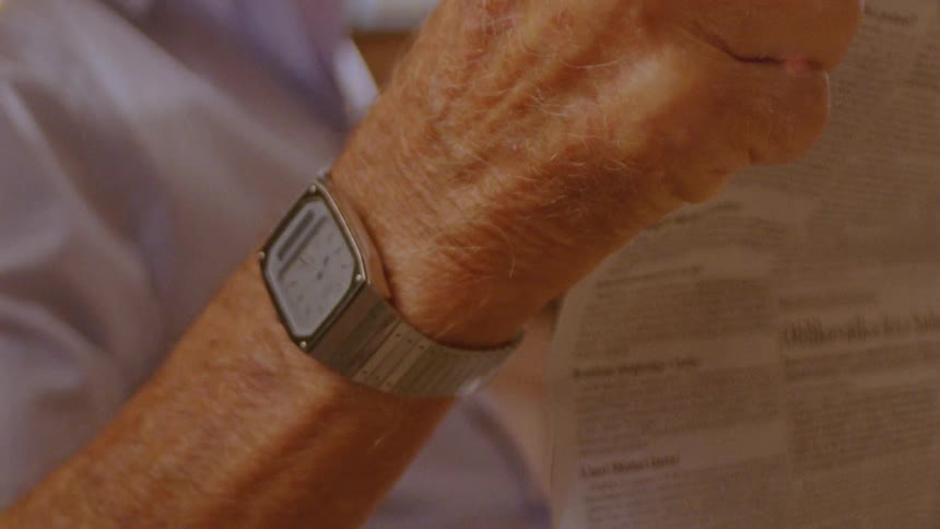 The hand of an elderly man wearing a wristwatch and holding a newspaper
