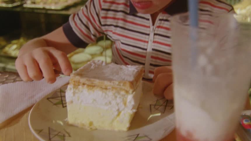 Child eating cake from a plate with a fork inside the kitchen