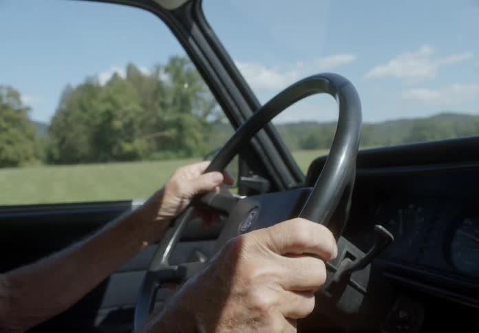 Closeup of hands on the steering wheel driving a car in a grassy environment