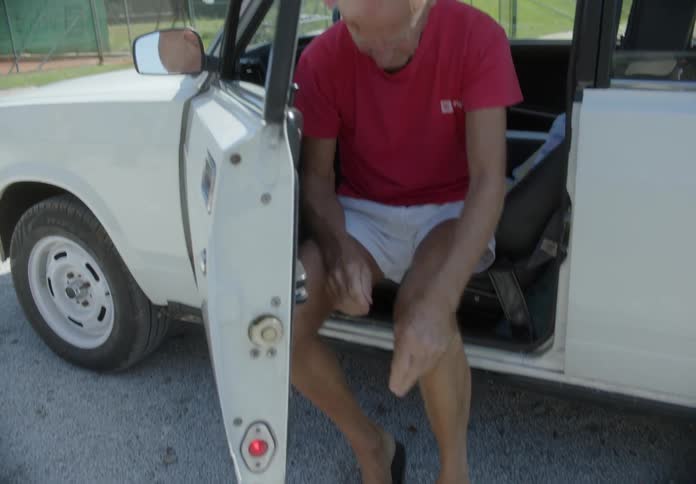 Elderly man sitting in the car seat with his feet outside wearing his sneakers