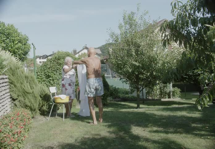 An elderly couple is hanging clothes on a clothesline in the garden