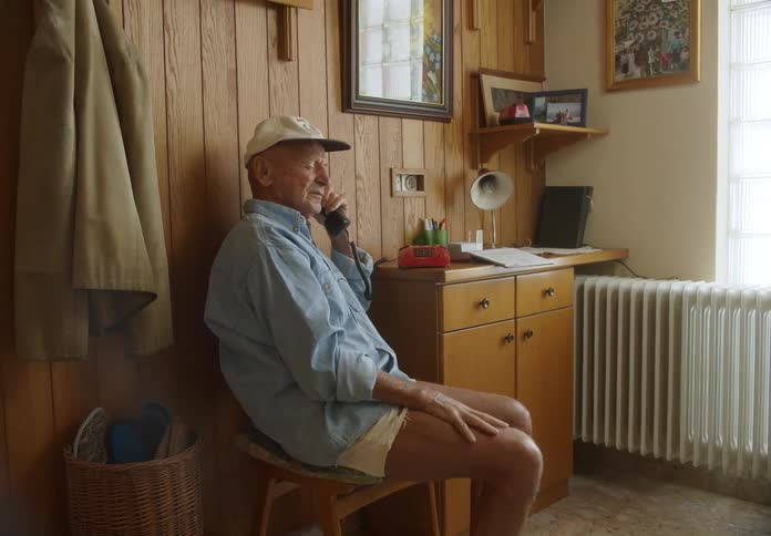 A man is sitting indoors and talking on a rotary phone