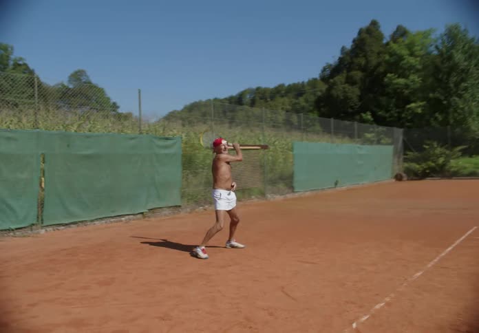 Tennis player returns ball while playing on tennis court next to crop field