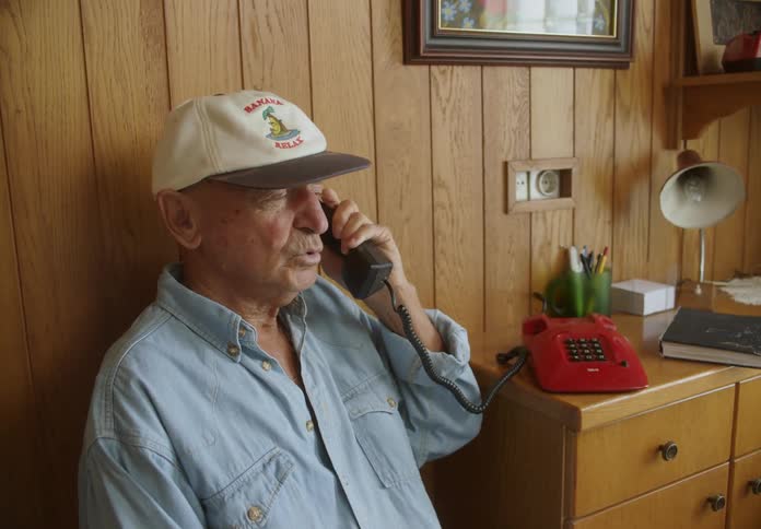 An elderly person answering the phone and sitting in the chair next to it while talking