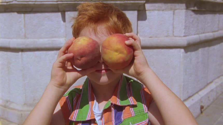 A boy reveals his face that was hidden behind two peaches he is holding