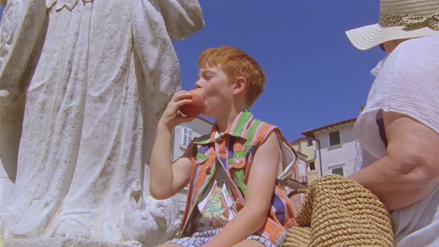 Boy eats while sitting a base of statue near mother