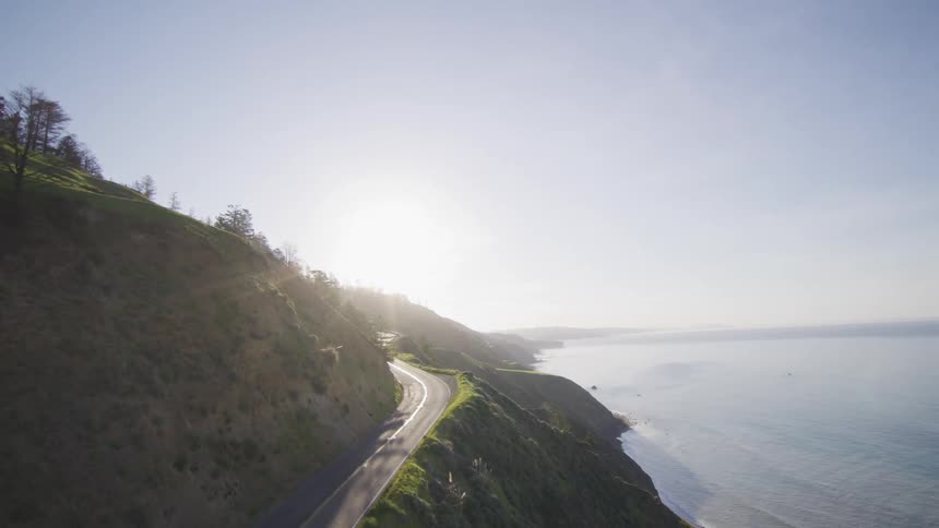 Drone view of a coastal highway with a car driving on a bright sunny day