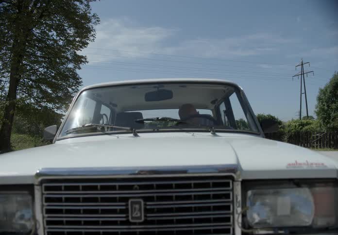 A car driving across a gravel parking lot on a bright sunny day as a it comes to a stop and a man steps out