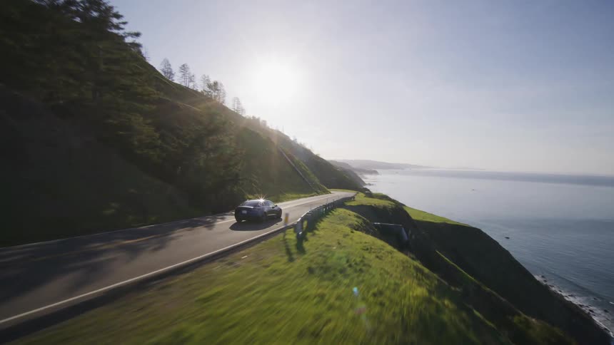 A car driving on a coastal highway at sunrise