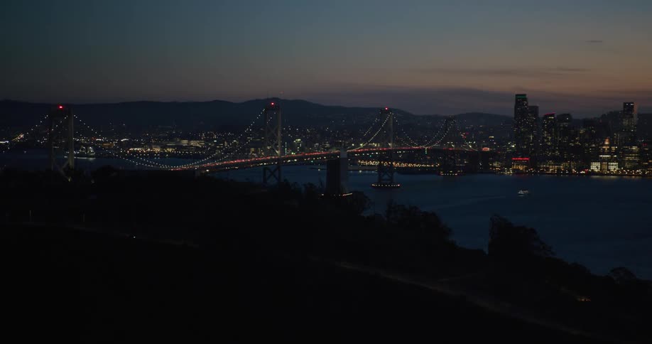 Drone view of the Bay Bridge lit up at night with the San Francisco city skyline lit up on the horizon