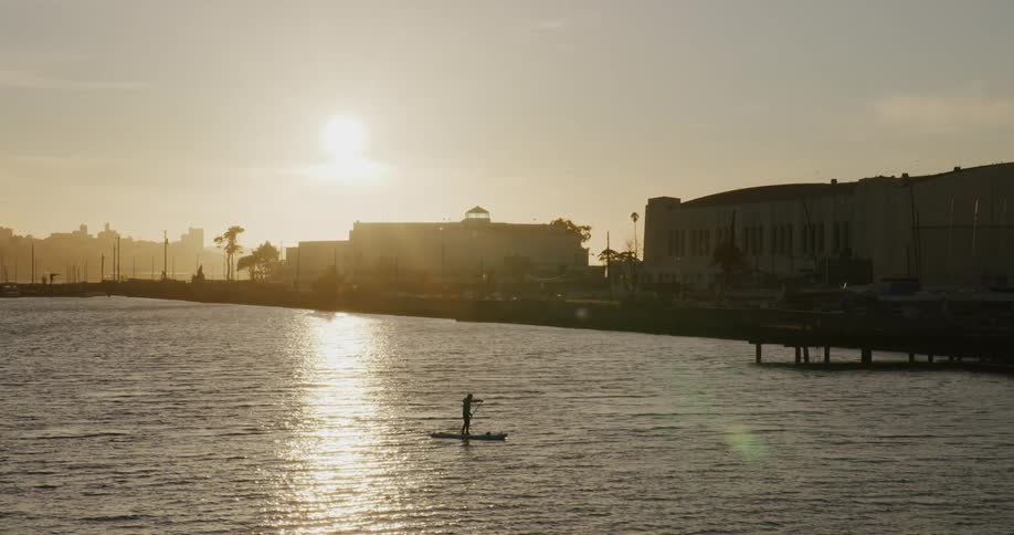 City skyline with the sunset in the background and a person standup paddling on the San Francisco Bay