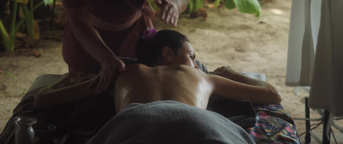 Woman lying shirtless receiving a massage in a natural environment