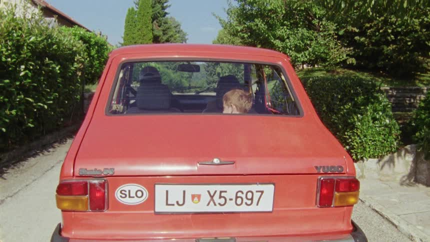 Boy waves goodbye before entering a red car in the countryside