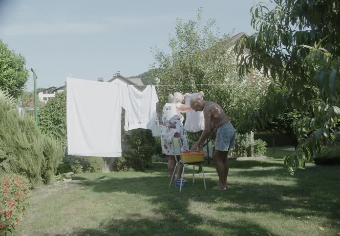 A man and woman hang clothes and sheets in their yard