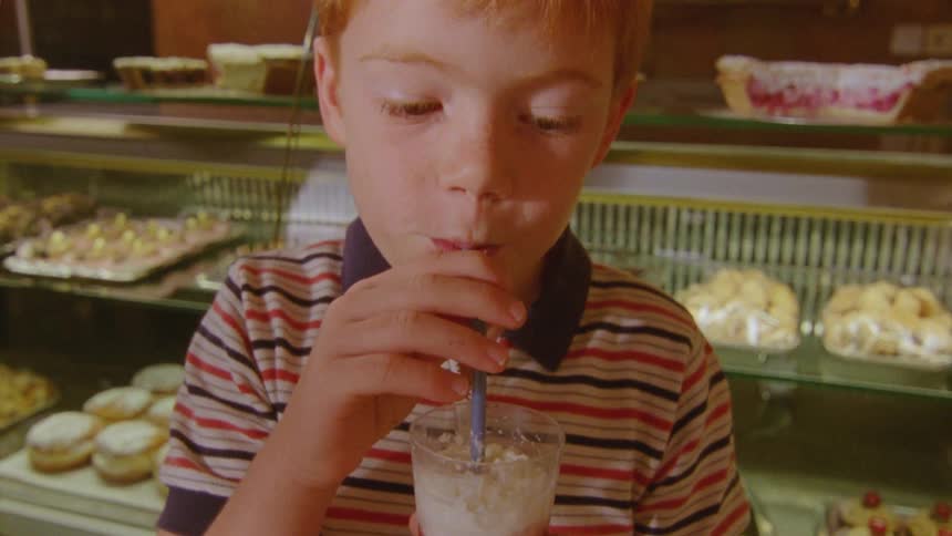 Child with a straw drinking a beverage containing whipped cream